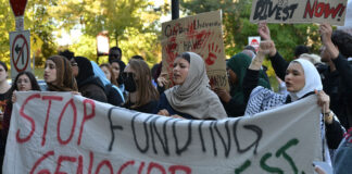 Opinion: Carleton’s investments in companies violating human rights clash with its own ethical guidelines. group holds banner saying 'stop funding genocide' and 'divest now'