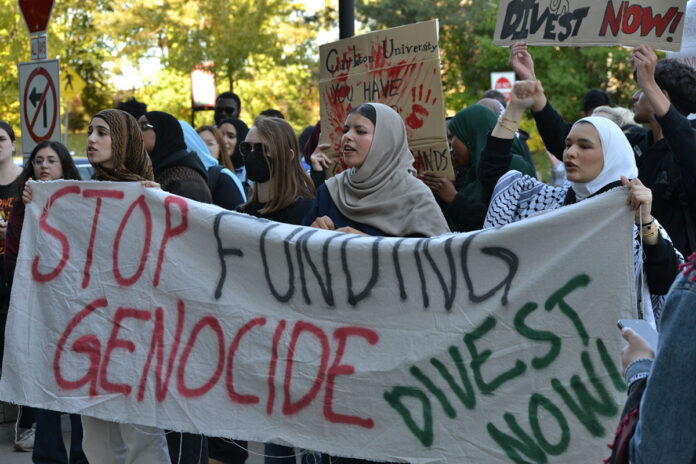 group holds banner saying 'stop funding genocide' and 'divest now'