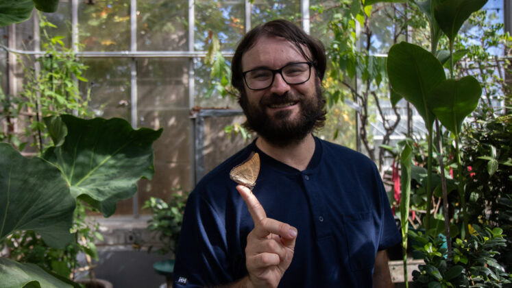 A man stands with a butterfly perched on his finger