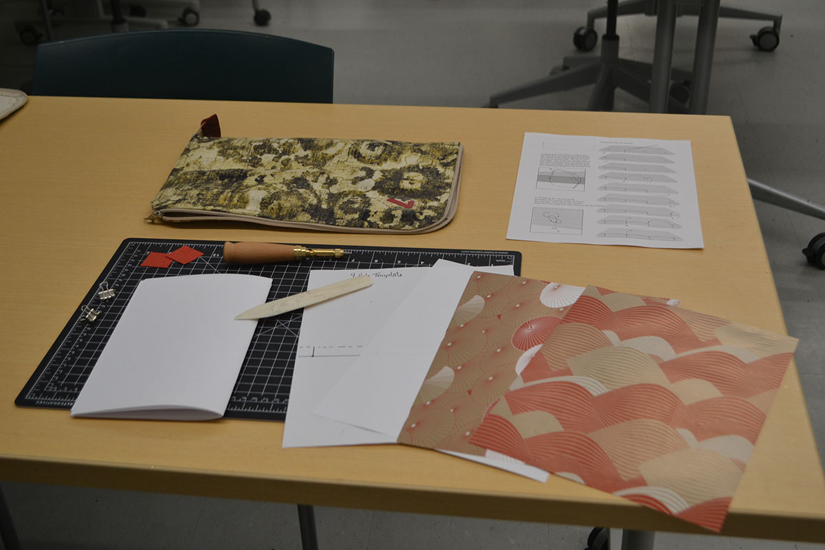 Different coloured papers, measuring tools, templates, and other tools lay on a table
