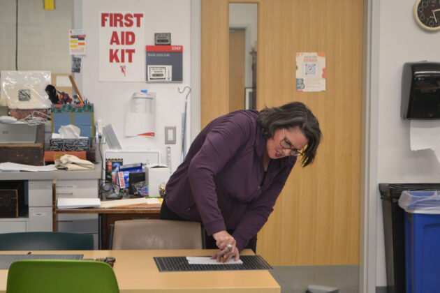 A woman twists a tool on a paper that is on a table in front of her.