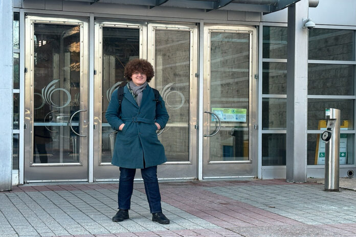 A person stands in front of silver doors with an O logo for the City of Ottawa on the doors