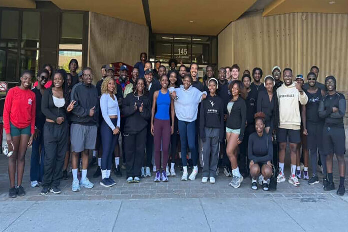 A group of dozens of people in athletic wear stand in front of a building