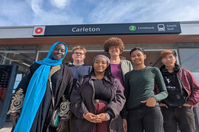 Six people stand in front of a sign with a red circle O-Train logo on it, the word 