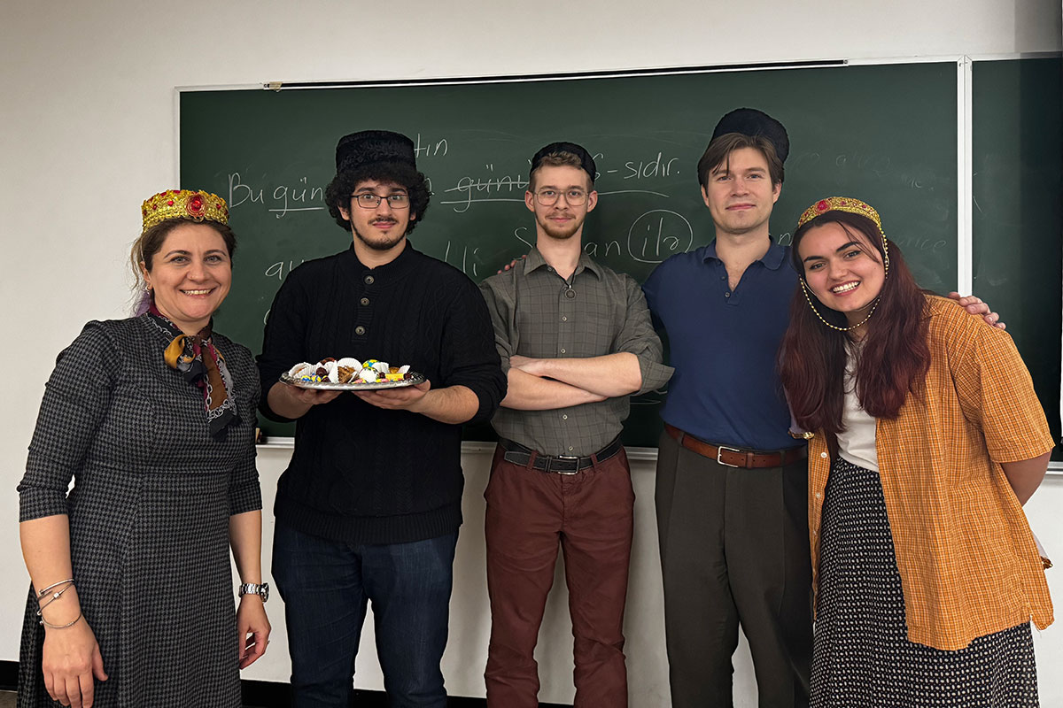 Five people stand in front of a chalkboard, with one holding a plate of food