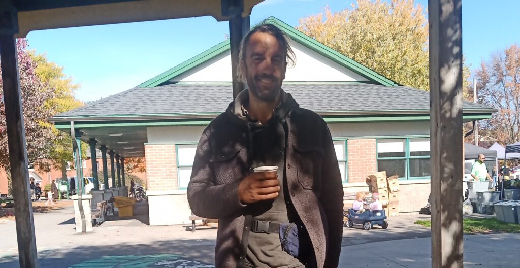 A man in a brown jacket holding a paper cup outdoors. 