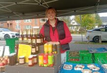 ‘Bad news’: Farmers’ markets face an uphill battle due to climate change and rising prices, Ottawa-area vendors say A woman standing in a red sweater and black jacket behind a stack of bottles.