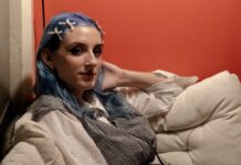 hannah vig looks to make space for underrepresented Ottawa artists A person with blue hair sits and looks at the camera against an orange-painted wall.