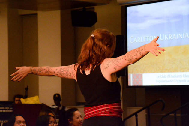 A person walks with their arms spread out in a tank top and tattoos of small designs on their arms