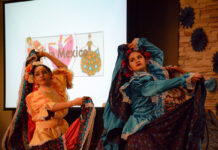 In photos: Carleton cultural fashion show returns after pandemic disruption Two people hold up their long skirts on their dresses up above their heads as they dance on a stage