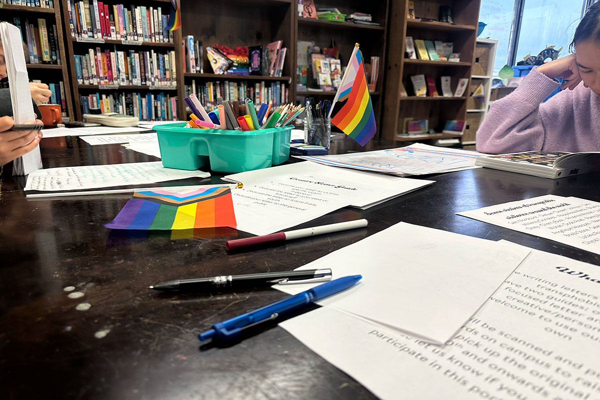 Papers, pens, markers, and pride flags sprawled on a table.