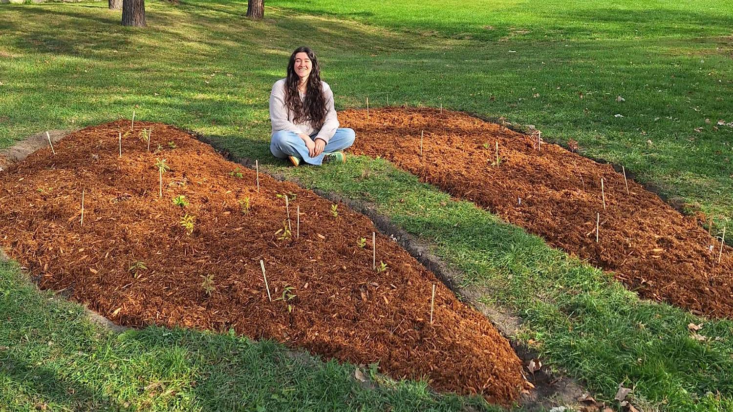 Woman sitting in open empty field where a new pollinator's garden has been planted. 