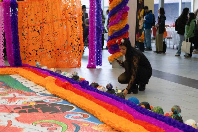 A woman kneels in front of an altar with painted skulls, laying down a flower in front