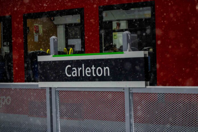 Carleton written on O-Train sign banner during a snow storm.