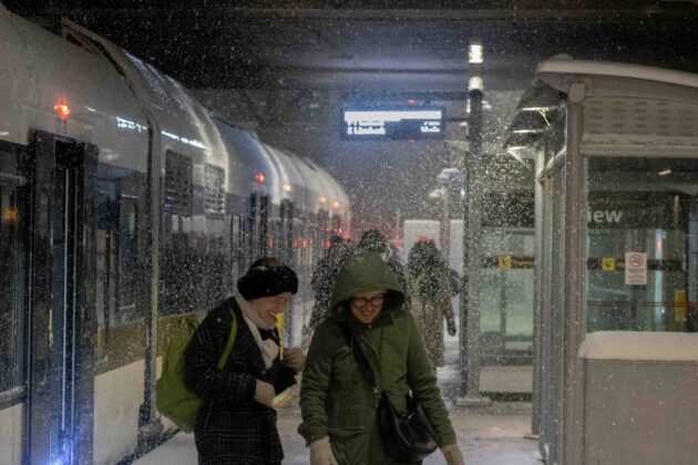 People smile and laugh as snow falls around them during a snowstorm.