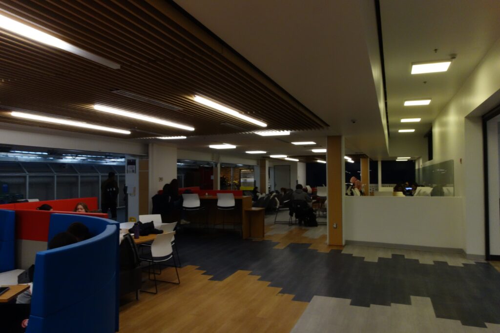 People study in the library, illuminated by overhead lights. 