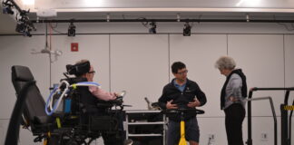 More than a decade on, Carleton research group is writing disability history Three people are gathered around a technological structure that is waist-height and includes handles.