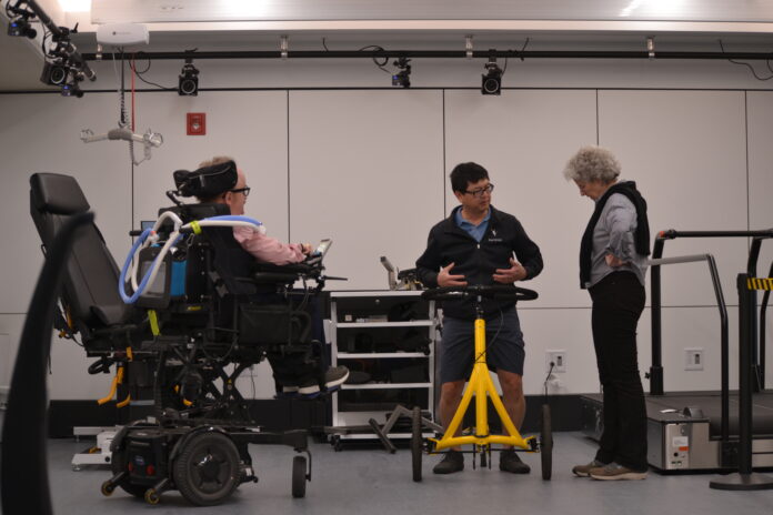 Three people are gathered around a technological structure that is waist-height and includes handles.