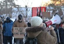 ‘Reject the gag order’: Students protest Carleton’s impartiality policy A person holds a megaphone to their mouth in front of a crowd of people, some holding signs, including one that says "reject the gag order"
