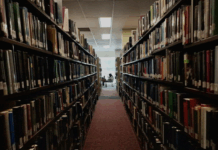 AI is booming. Here’s what universities are doing to keep writing alive Rows of bookshelves in a library and a student studying in the distance