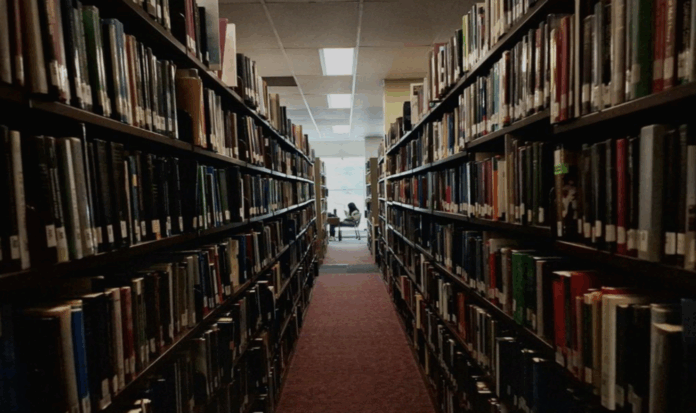 Rows of bookshelves in a library and a student studying in the distance