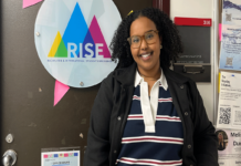 Q&A: To this social worker, micro-aggressions are like ‘silent attacks on our body.’ And they add up. A person stands in front of a door with a sign that says "RISE: Racialized & International Student Experience"