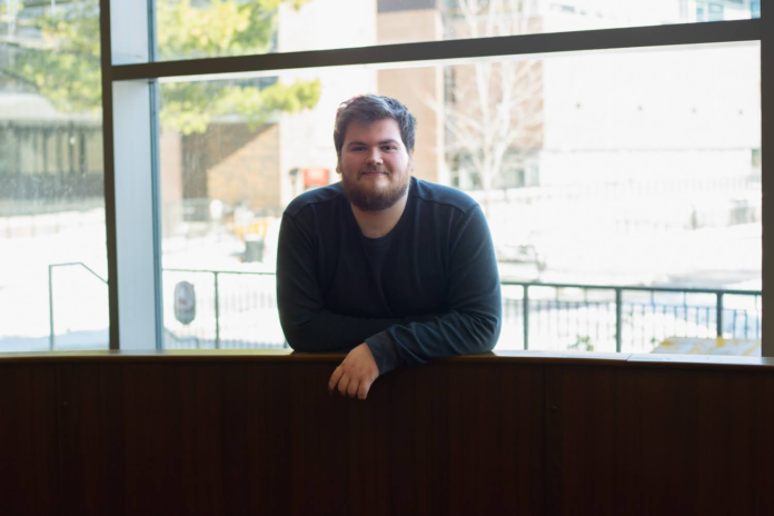 Maxwell Heroux poses for a picture in front of a window.