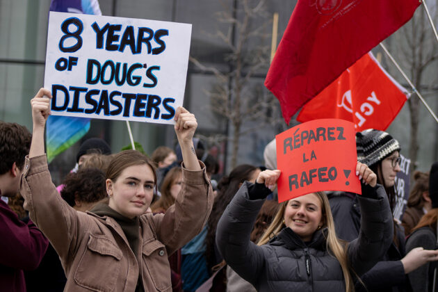 Students stand in a crowd. One person holds a sign saying "8 years of Doug's disasters" and another holds a sign saying "R&eacute;parez la RAFO"
