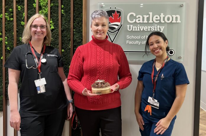 Three women - one in black, another in red and another in blue scrubs standing in front of a Carleton University sign.