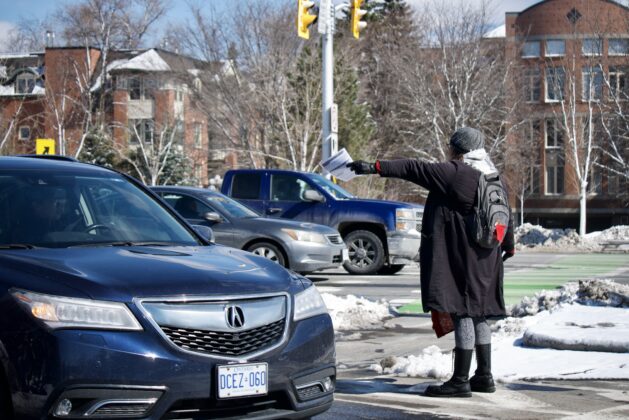 Person handing out a pamphlet near a black car