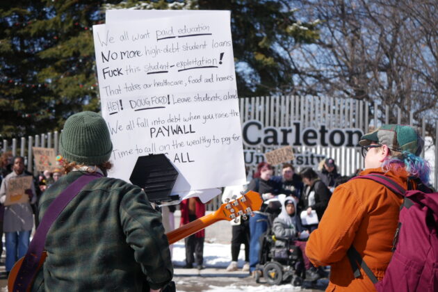 Person holding a sign with the Carleton University sign in the background