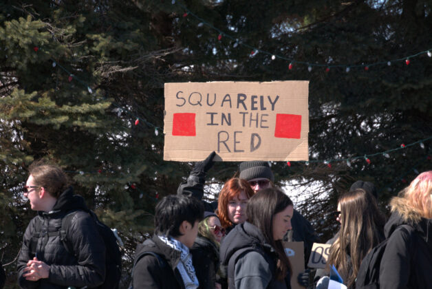 Person holding up a sign that reads "Squarely in the red"