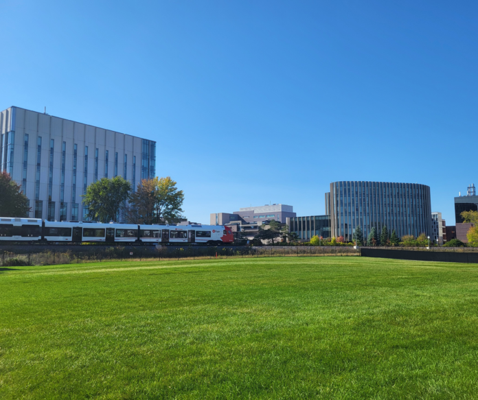 P9 IMAGE - Steven Reid Train goes by in a field of green at Carleton University campus