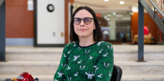 Q&A: Meet the Carleton researcher tracing disability justice history — and proposing a brighter future A woman sitting on a mobility scooter is in front of stairs in a hall