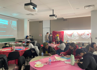 ‘Love as resistance’: Students write letters to political prisoners in the Philippines About a dozen people stand around or sit at several tables decorated with table cloths and filled with papers and writing materials. Some people talk to each other, some are writing on their papers.