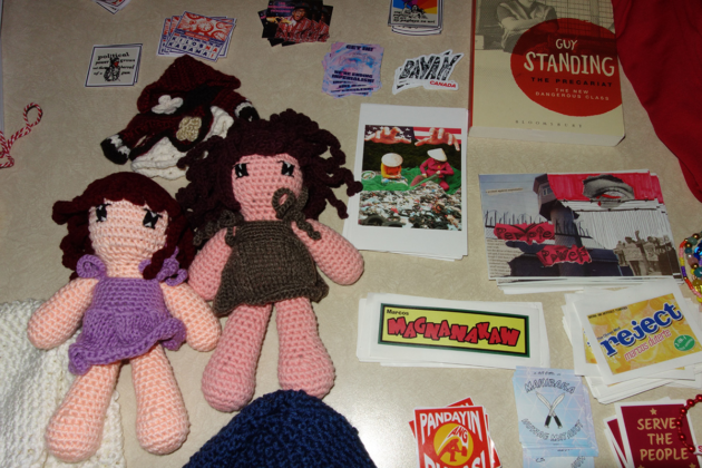 Two knit or crocheted dolls lay on a table that has graphic stickers and a book with the title "Guy Standing"