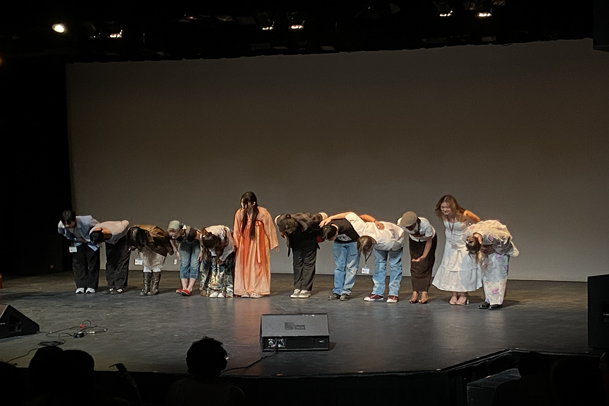 Twelve people bow on a stage