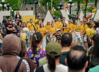 Ottawa’s largest Brazilian festival showcases cultural traditions and community spirit image displaying a crowd a people mostly dressed in yellow smiling and holding drums in front of an Ottawa sign in Ottawa.