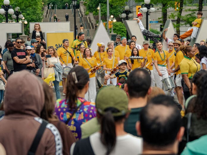 image displaying a crowd a people mostly dressed in yellow smiling and holding drums in front of an Ottawa sign in Ottawa.