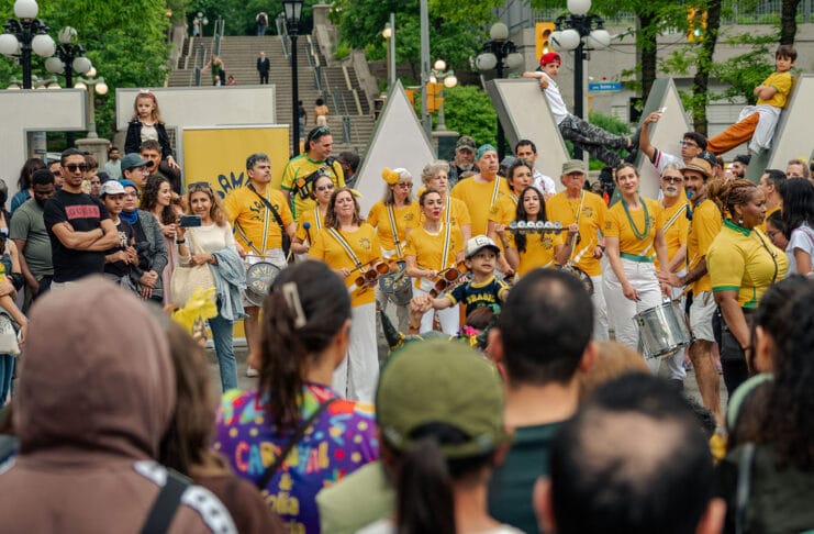 Ottawa’s largest Brazilian festival showcases cultural traditions and community spirit image displaying a crowd a people mostly dressed in yellow smiling and holding drums in front of an Ottawa sign in Ottawa.
