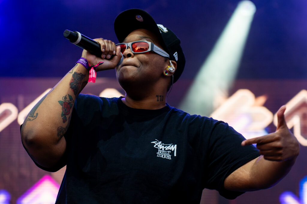 Person holds mic close to face with shades on while rapping on stage.