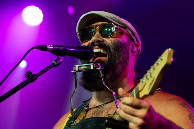 Man smiles while singing into microphone with shades on