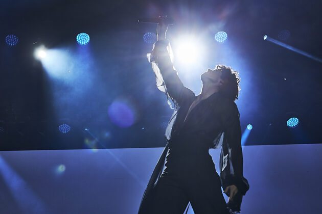 Man raises mic to the air while looking up on stage