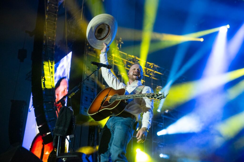 Man raises cowboy hat with guitar around him