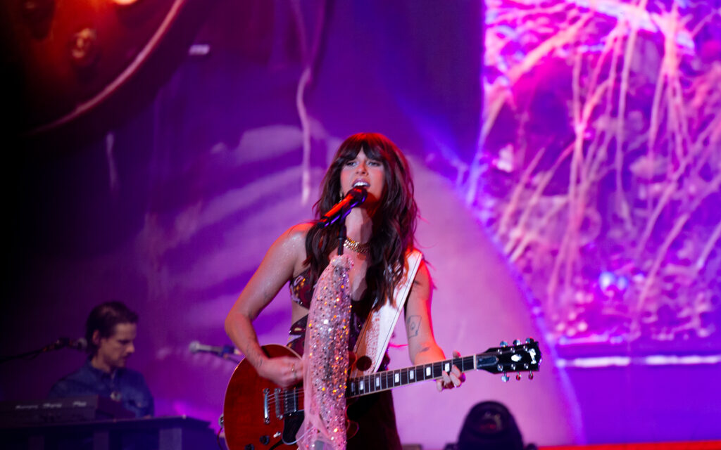 Woman strums guitar while singing on stage