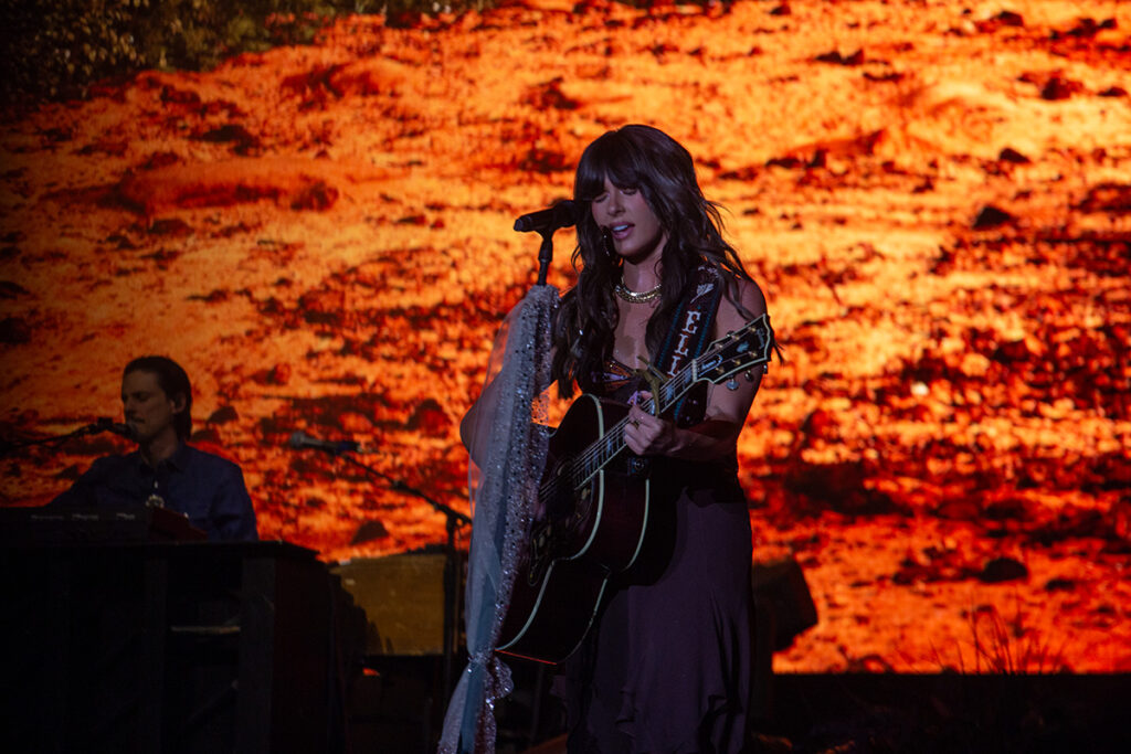 Woman closes eyes while singing into microphone with guitar