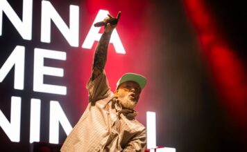 Bluesfest Day 2 review: Limp Bizkit brings the house down with metal nostalgia and a hometown surprise Man raises arm with microphone on stage with song lyrics behind him