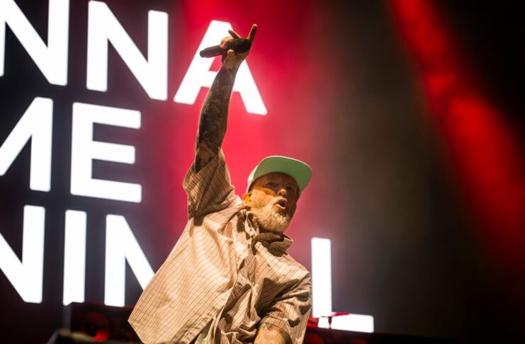 Bluesfest Day 2 review: Limp Bizkit brings the house down with metal nostalgia and a hometown surprise Man raises arm with microphone on stage with song lyrics behind him