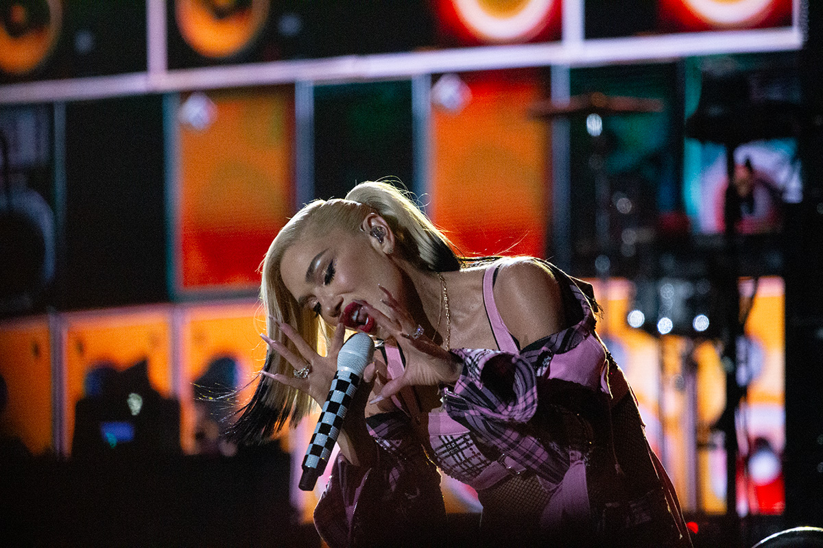 GwenStefani3 Woman sings into mic while kneeling down on stage