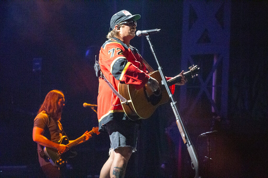 Man wears cap and Sens jersey while playing guitar and singing